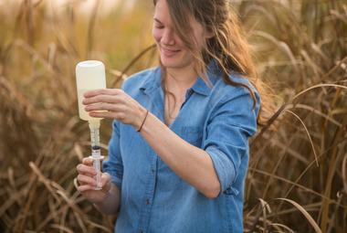 A woman pours water from a larger sampling bottle into a smaller one.